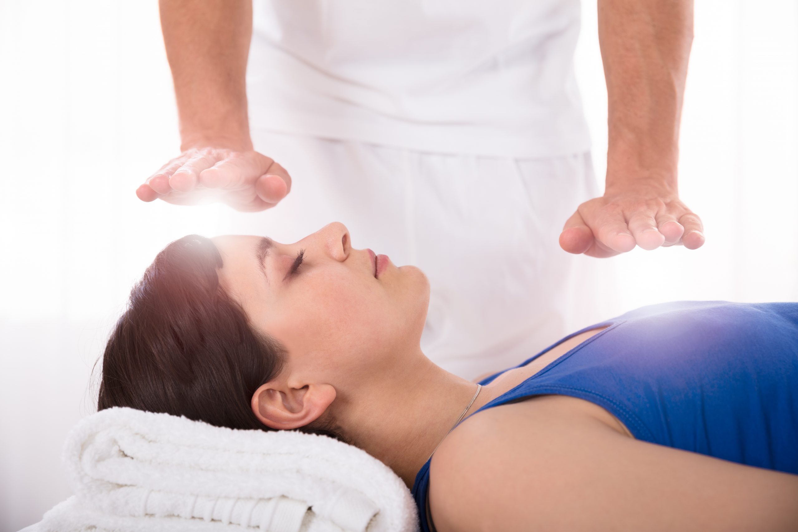 woman lying down receiving reiki energy healing through the hands of a practitioner
