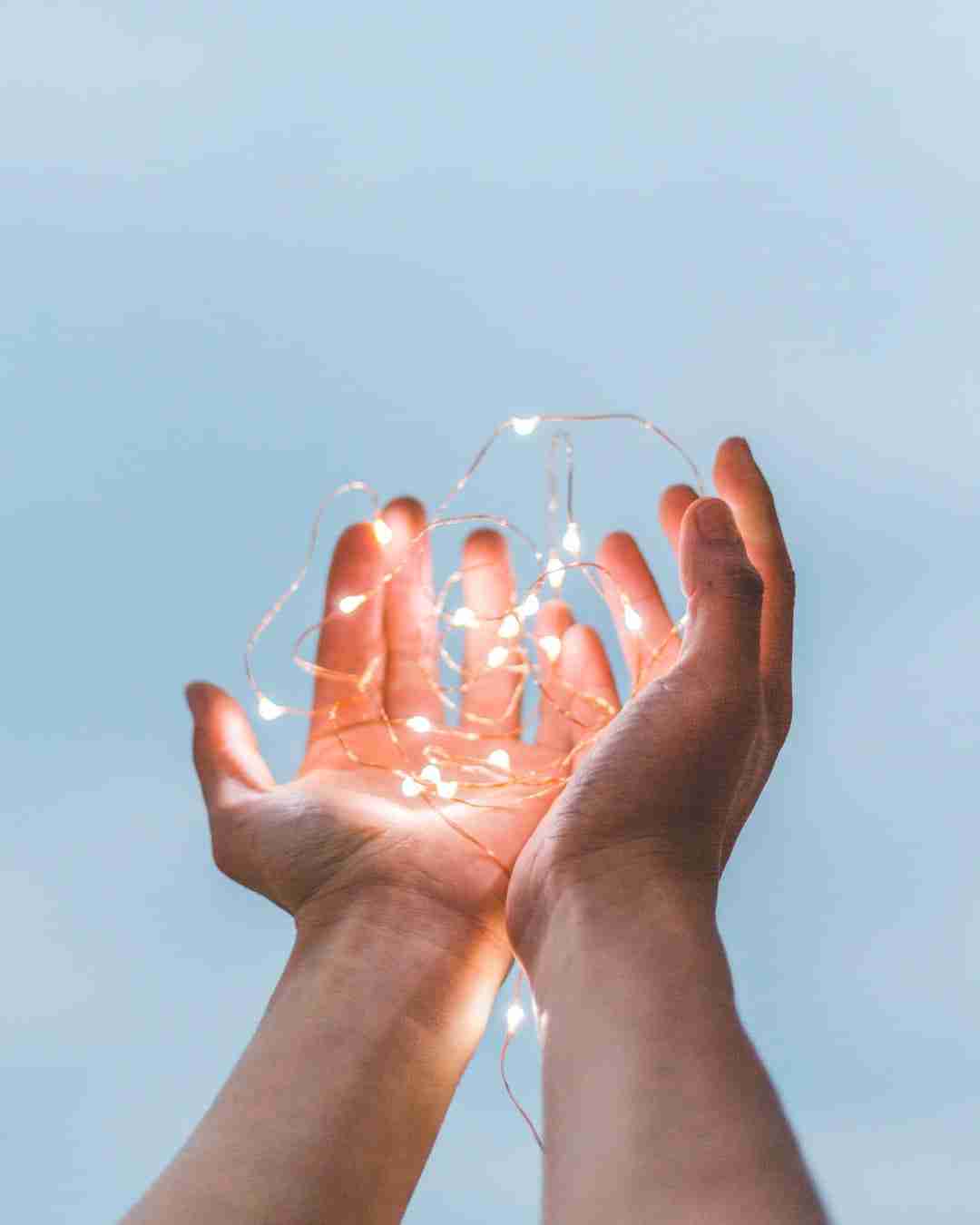 Hands holding a bunch of small illuminated lights indicating the healing energy of the hands