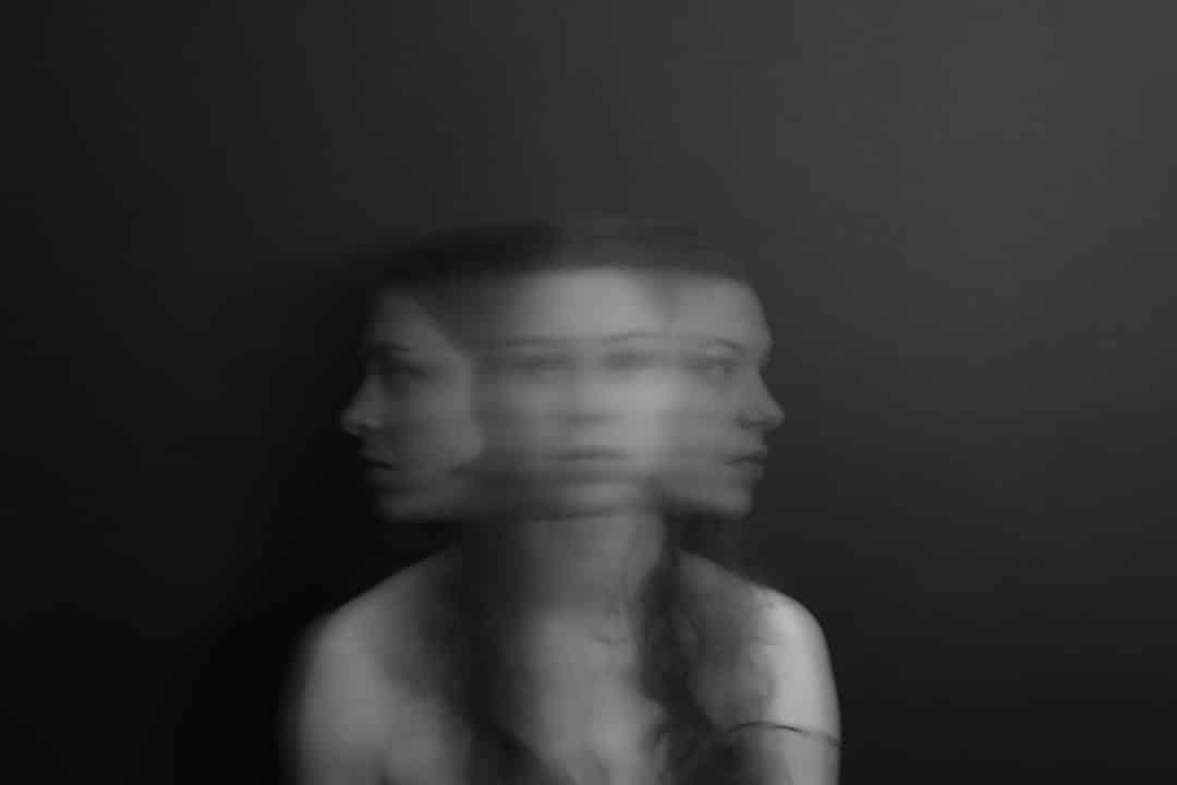 An anxious young girl sitting still with two, blurry side profile images of her face next