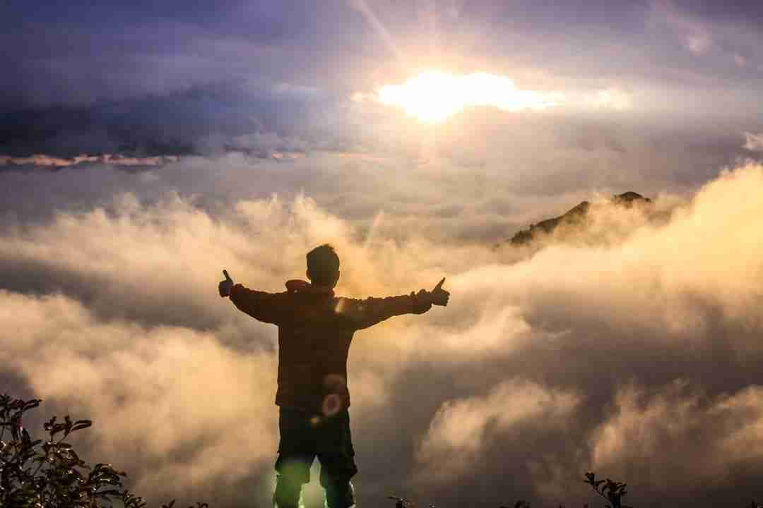 A man rising above the clouds into the sunlight with arms extending out and giving two thumbs up as to have gained immense clarity